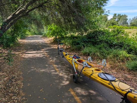 My fold-up bike connected to my modular kayak cart. Pictured on a paved bike trail shaded by trees.