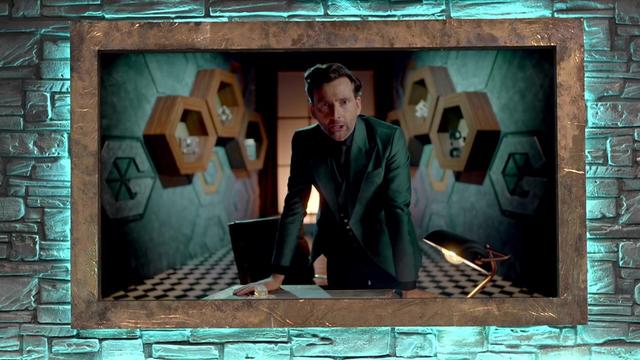 David Tennant stands up and leans on a desk while he addresses the camera. He's in a small study, lit in a greeny-blue, with a checkerboard floor and wooden hexagons on the wall. The same wood surrounds the telly set on which we see David, and the same shade of green is on the wall around the telly.