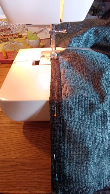 wir schauen auf die Nähnadel einer Nähmaschine, dort ist ein dunkelgrün/blauer Stoff schon eingelegt und wird gleich zusammen genäht