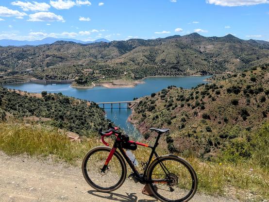 View of a lake from the top of a hill with mountains in the background. My bike is standing in the foreground.