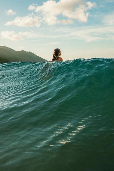 Woman riding a wave with a mountain in the background.