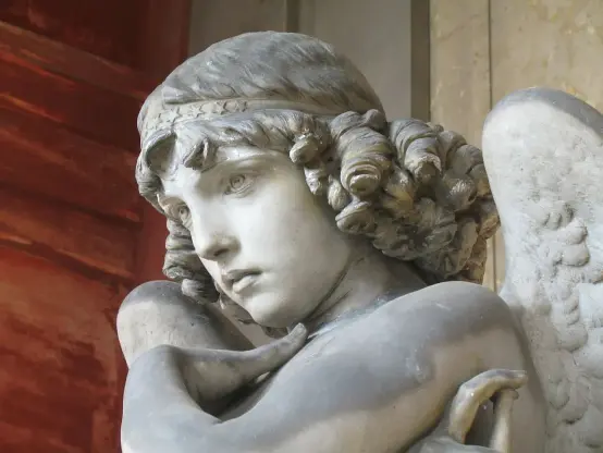 The image depicts a marble statue of an angelic figure, characterized by a thoughtful expression, curly hair, and wings. The figure's pose is contemplative, with arms crossed, and it displays intricate details typical of classical sculpture. The background suggests a historic or architectural setting, possibly indicating the statue's placement in a museum or historical site.

Image Credits: Wikimedia / Twice25 &amp; Rinina25 / CC BY 2.5