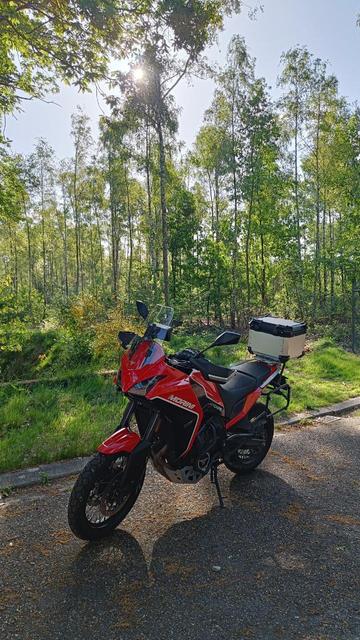 A red motorcycle parked on the tarmac, lush green trees in the background