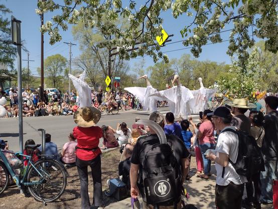 A group of large puppets in the shape of large white birds dancing in a street parade.