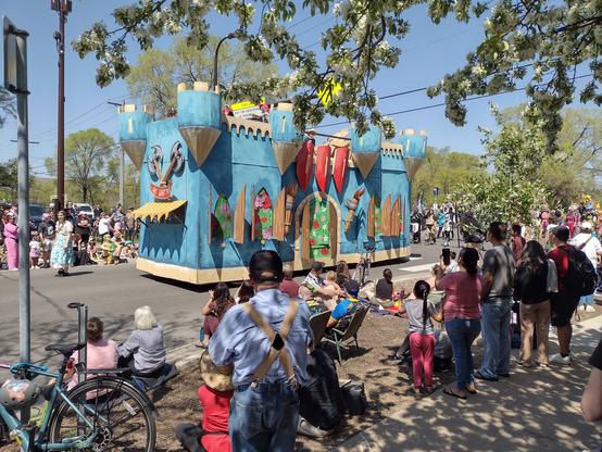 A large parade float in the shape of a huge blue castle  on a city street.  The float is at least two stories hight.