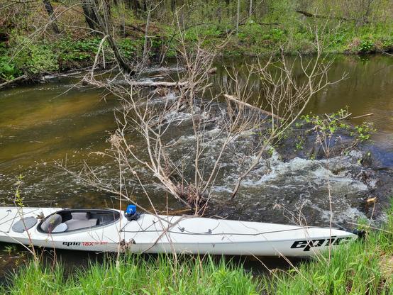 Water rushing over sticks across a 20-foot stream.  In the foreground is a white kayak.