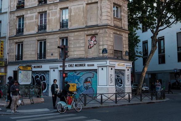 A street scene with people outside a corner building featuring graffiti and a small pixel art on the wall.