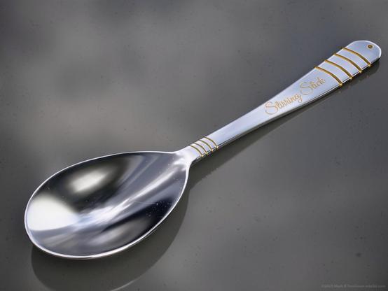 Silver spoon with gold trim and a label engraved Stirring Stick.