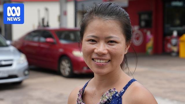 A portrait shot of a young woman in a blue dress standing in front of cars in a carpark.