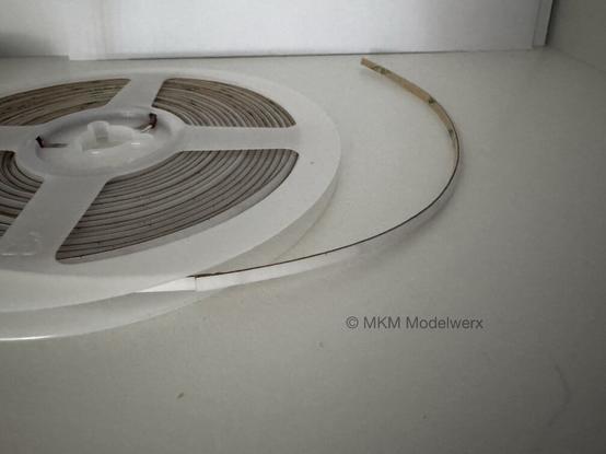 A reel of very thin blue LED light strips on a white shelf.