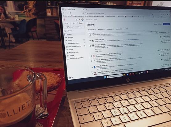 Ordinateur portable affichant l'interface de projets sur LaForgeÉdu, avec un café et un cookie sur une table en bois dans un café cosy.