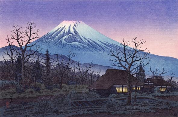 Sunset, looking toward Mount Fuji from a farm in Susono, Shizuoka. In the foreground, trees are bare, waiting for spring. A pair of farmhouses, one with a traditional thatched roof, have been closed up for the evening; warm light glows in their windows. Nearby, rectangular vegetable patches have been sown in tidy rows, but have yet to develop much. Beyond, forests and foothills lead toward a snow-capped Mount Fuji, still shining in a sky turned purple and pink with the setting sun.