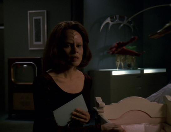 B'Elanna sits next to her unborn baby's crib, with a toy Klingon Bird-of-Prey in the mobile over the crib.