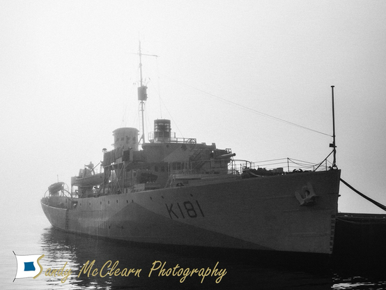 Small historic warship alongside against a foggy background.