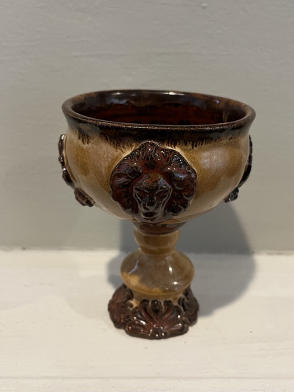 A raised lions’s head adorns the side of this bulbous bodied goblet. The lion, and fan leaves around the flared base, and glazed with Copper Float - a dark, rusty variegated reddish brown - as is the rim and interior bowl of the vessel. The body and handle are glazed with Kim’s Orange Brown - a mottled creamy caramel color.