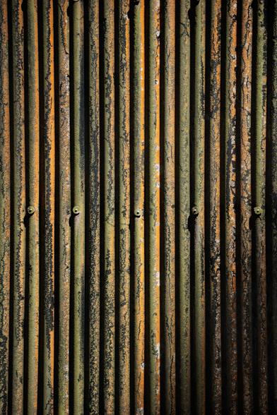 Vertical metal panels with a weathered texture showcasing hues of orange, green, and black, hinting at age and rust. Fixing screws visible.
