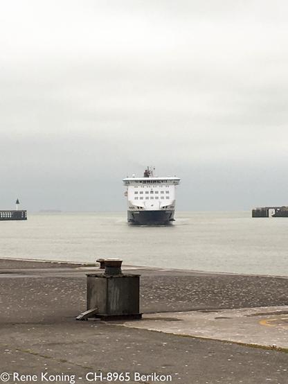 Eine Fähre lauft in den Hafen ein. Mann sieht das Schiff frontal von Vorne, die Weisse Brücke dominiert. Im Vordergrund ist die Kaimauer zu sehen und im Hintergrund links und rechts die Molen beim Hafeneingang