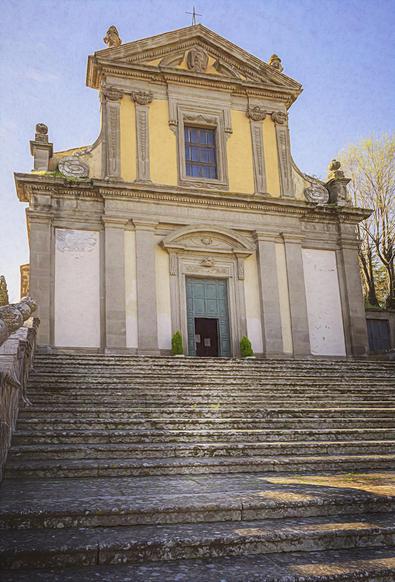 An elegant stone staircase leads to the entrance of the Church of San Pietro in Viterbo Italy. The exterior is adorned with decorative columns, ornate carvings, and a triangular pediment at the top. It was a little worn but still attractive.