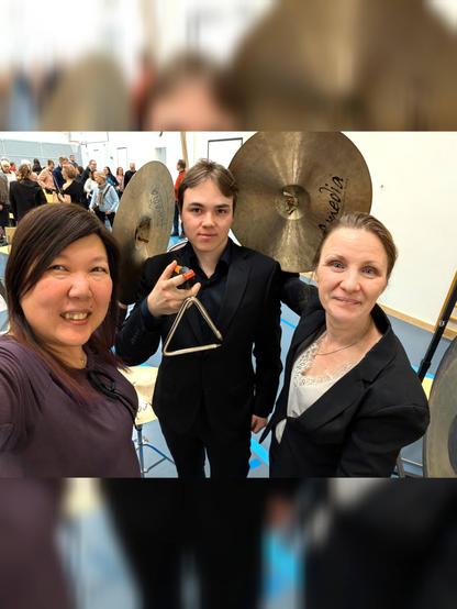 Three percussionists goofing around with a pair of crash cymbals and a triangle after the concert.