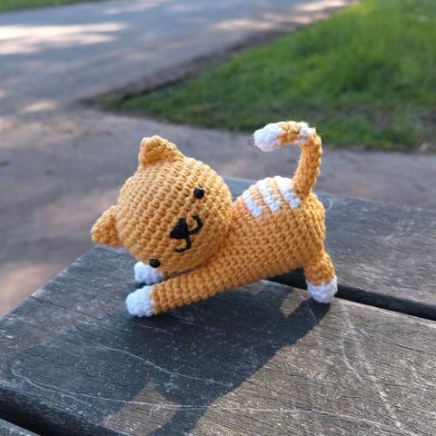 A picture of an orange/white crocheted cat on a picnic table outside.