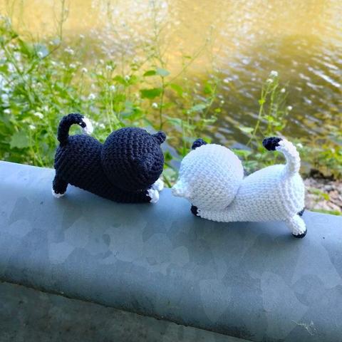 A picture of a crocheted white and a crocheted black cat outside, across from each other, heads pointing towards each other.