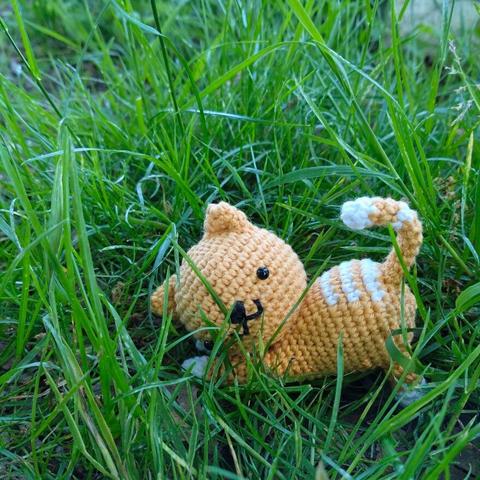 A picture of an orange/white crocheted cat in grass.