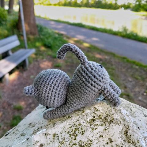 A picture of a crocheted grey cat on a white fence post.