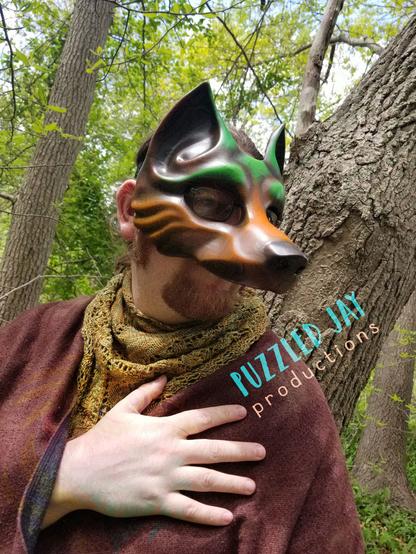 people wearing a brown and green wolf mask peer around trees