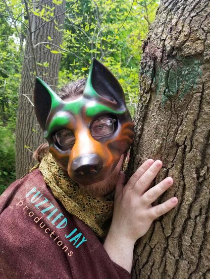 people wearing a brown and green wolf mask peer around trees
