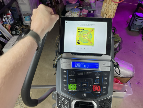 Elliptical machine with iPad mounted on it playing the Hard Fork podcast
