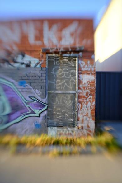 Graffiti adorns a screen door on a brick building in a local laneway