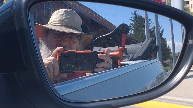 Ich mit Hut, mein orangenes Händi und mein orangenes G-Line spiegeln sich im Aussenspiegel von Ventys weissem Beetle Cabrio.