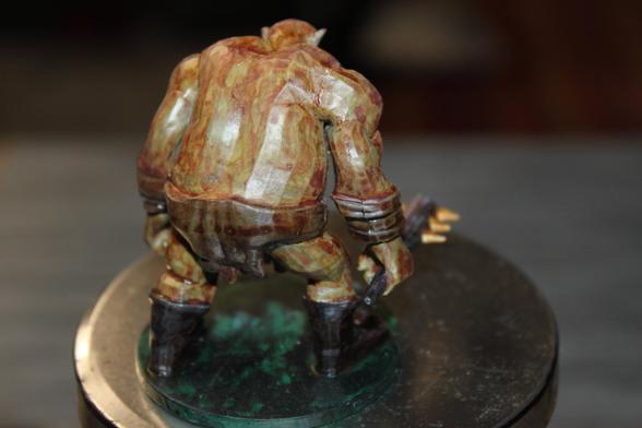 Alt Text (Rear View):
Rear view of the same ogre miniature, showing its broad muscular back, leather loincloth, and bracers. The figure's posture is hunched forward, with the spiked club lowered behind it, all mounted on a green circular base.
