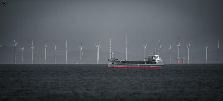 monochrome shot of cargo ship in front on sea windturbines