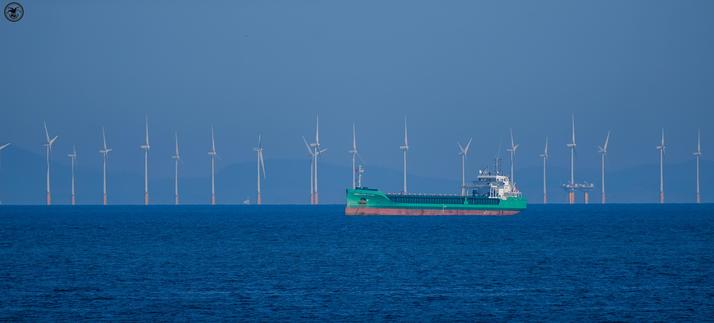 cargo ship out on ocean in front of windturbines