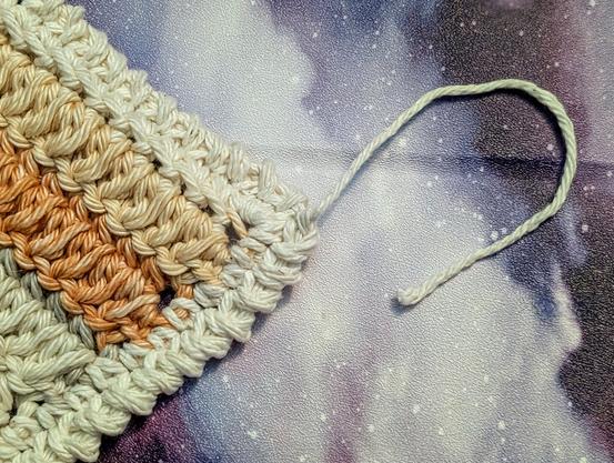 A close-up of the corner of a crochet dishcloth with the tail just laying there because it's too lazy to sew itself in.