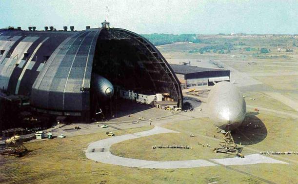 Two blimps are seen. One is in the hanger, the other is outside.