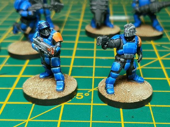 A photo of partially painted miniatures. 2 are in focus, sci-fi armoured soldiers in very vibrant blue.