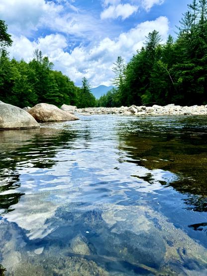 Photo of distant mountain peak as viewed from reflective calm river. Reflections of overhead blue sky and white puffy clouds can be seen on surface of water. Large boulders line the river.

East Branch Pemigewasset River with view toward the Bonds (a range of peaks in the Pemigewasset Wilderness). White Mountains, New Hampshire.

I took this pic on a backpacking trip on July 15, 2024.