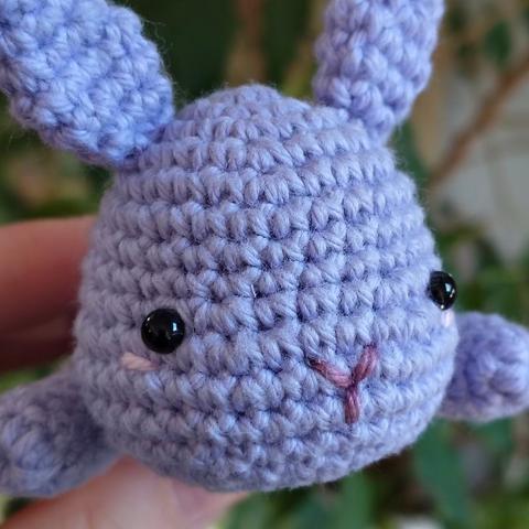A close up of a lilac crocheted bunny with embroidered pink cheeks.
