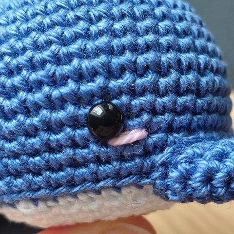 A close up of a crocheted whale with embroidered pink cheeks under its eyes.