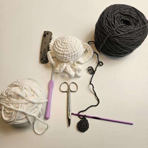 a white octopus shaped creature woth grey yarn ready and started on the bottom side.