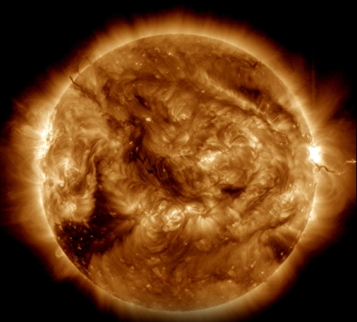 The solar disc, seen in a special filter by the SDO satellite. This surface of the Sun in this image is turbulent and knotty. The colour of the twisted light is gold with dark brown patches. To the right, on the limb, an extended structure emerges from the surface and extends into space.