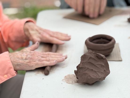 Hands rolling a snake or coil of clay with a lump of unused clay to one side and the beginning of a small coil pot on the other.