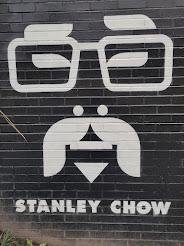 A face drawn on brock with the name of the artist Stanley Chow below it.