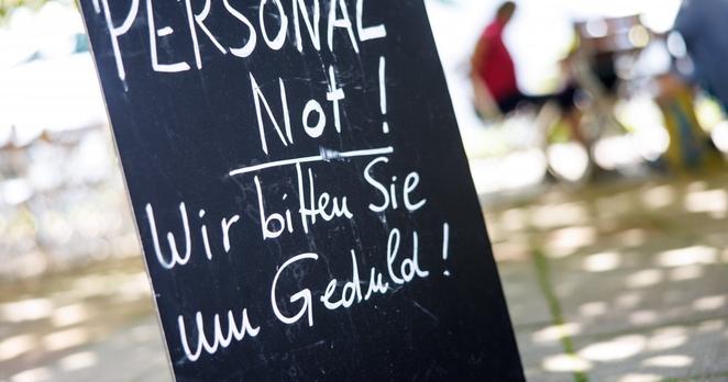 Auf einer Tafel am Eingang zu einem Biergarten steht „Personalnot! Wir bitten Sie um Geduld!“. Wie vielerorts fehlen auch hier Arbeitskräfte.