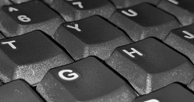 Close-up of a computer keyboard, seen diagonally from above. 6 keys are fully visible, with partially visible keys around the edge. They&#39;re dark gray with white markings, and close enough that you can see the texture on the sides of the keys and an outline around each letter suggesting that they were attached as stickers.