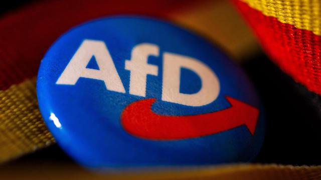 Symbolfoto AfD:Ein Ansteckpin mit dem Parteilogo der AfD (Alternative fuer Deutschland) liegt mit einer Deutschland-Banderole auf einem Tisch.