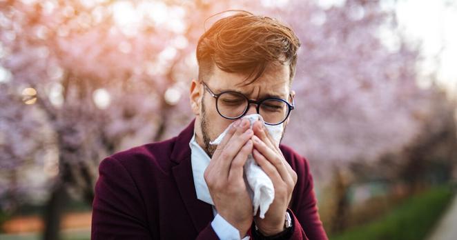 Young businessman sneezing in park.
