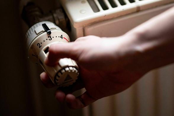 Eine Hand dumfasst den Temperaturregler eines Heizkörpers Eine Hand dumfasst den Temperaturregler eines Heizkörpers